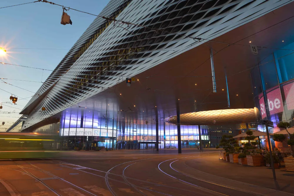 Messe Basel at dusk, a tram passing the lit facade.