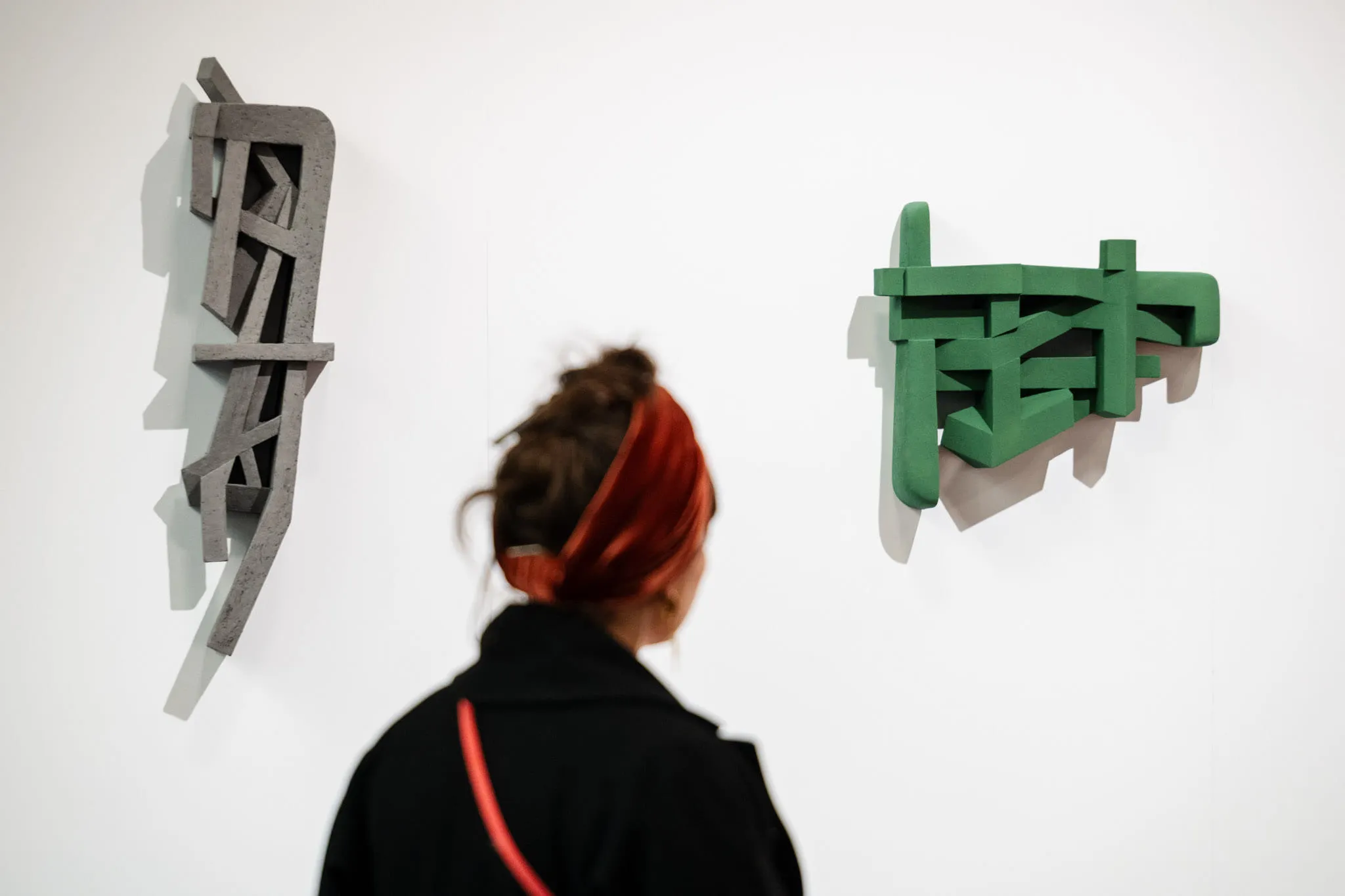 A visitor in front of two abstract wall sculptures, one grey, the other green.