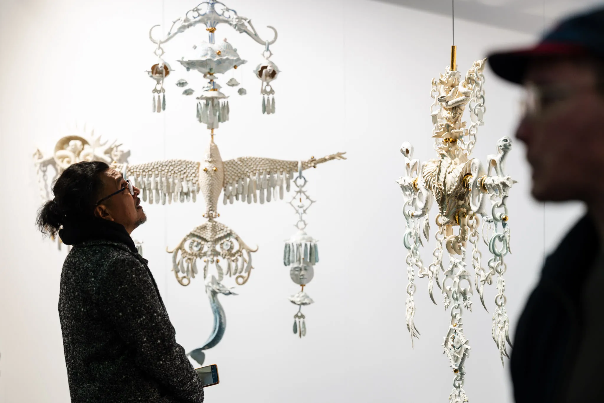 Visitors in front of finely worked white ceramic hangings, among them a bird with its wings spread.