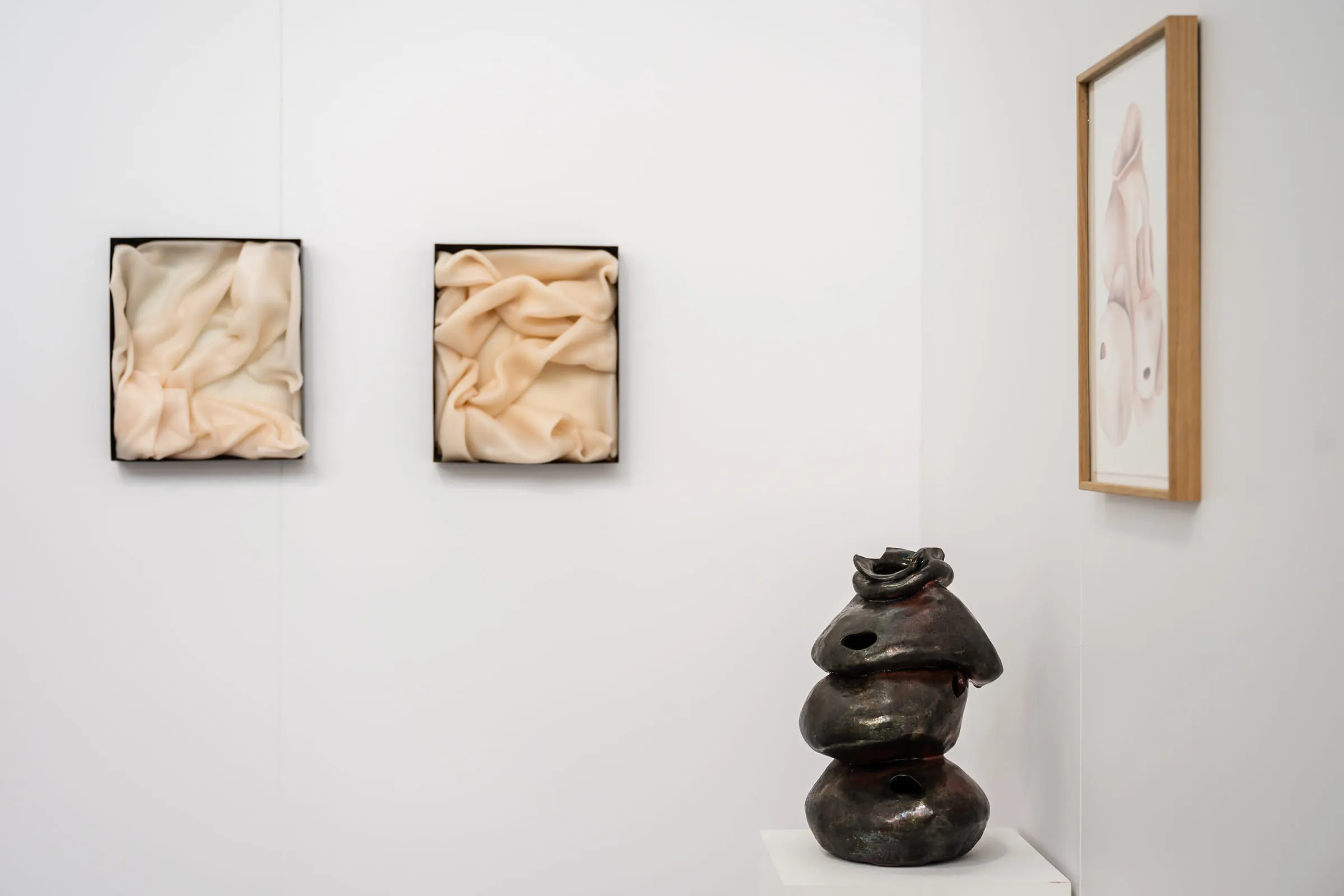 Deux reliefs clairs encadrés au mur et une sculpture céramique sombre faite de volumes empilés.