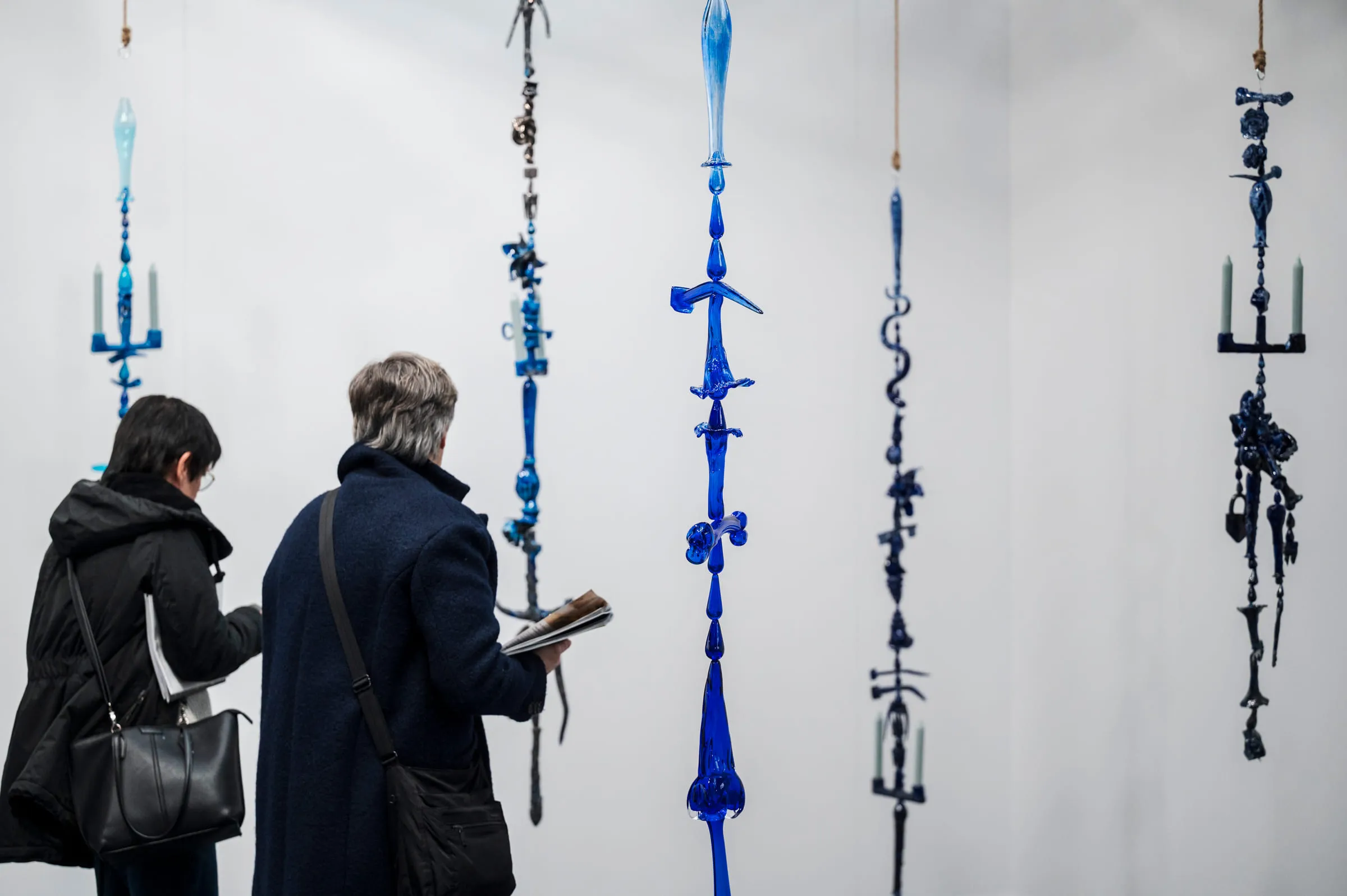 Deux visiteuses devant de longues suspensions de verre bleu accrochées au mur.
