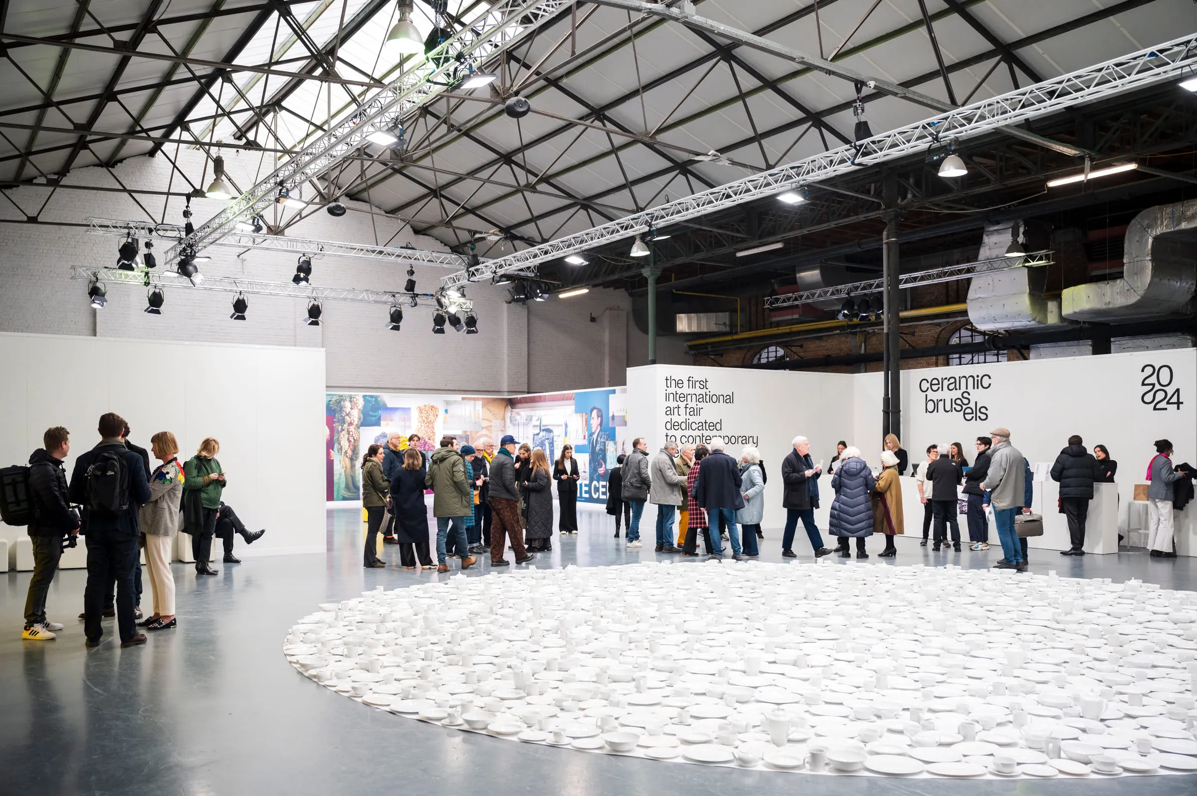 A large circle of white plates laid on the floor at the entrance to the fair, visitors standing around it.