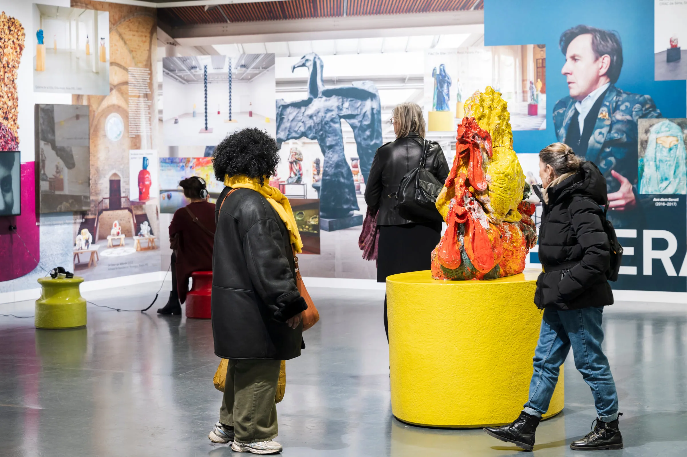 Visitors around a red and yellow ceramic sculpture on a yellow plinth.